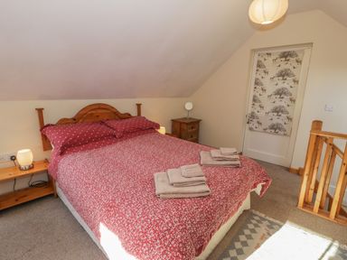 A bedroom with a bed with red bedding two bedside tables towels on the bed and a door with animal patterned curtain at Bryn Melyn Artists Cottage Llanelltyd near Dolgellau