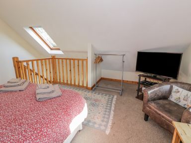 A bedroom with a bed and folded towels near a wooden railing a chair and a television at Bryn Melyn Artists Cottage Llanelltyd near Dolgellau