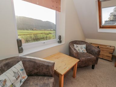 A room with two armchairs a wooden table a window with a view of fields and hills and a wooden chest at Bryn Melyn Artist's Cottage Llanelltyd near Dolgellau