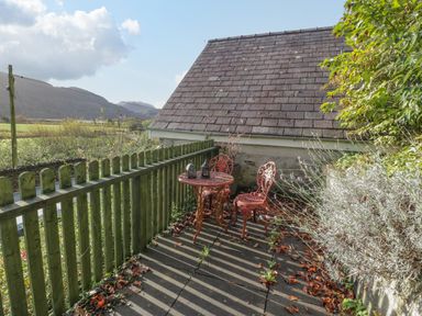 A small outdoor patio with a red metal table and two chairs next to a wooden fence and a stone building at Bryn Melyn Artist's Cottage Llanelltyd near Dolgellau