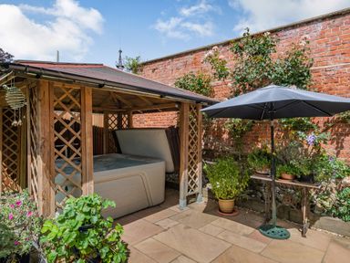 An outdoor patio area with a wooden gazebo housing a hot tub and a table with potted plants and an umbrella at The Lodge in Coltishall