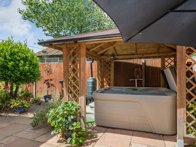 An outdoor patio area with a hot tub under a wooden gazebo surrounded by plants and a fence at The Lodge in Coltishall