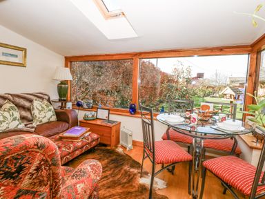 A living area with a sofa table lamp and glass dining table with four chairs by large windows at The Lodge in Coltishall