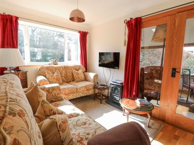 A sitting room with patterned sofas a small wooden table a wall mounted television and red curtains at The Lodge in Coltishall