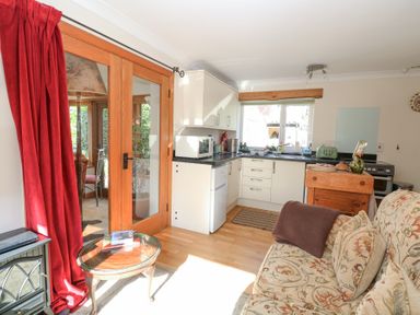A small kitchen and living area with floral sofa red curtains and wooden framed glass doors at The Lodge in Coltishall