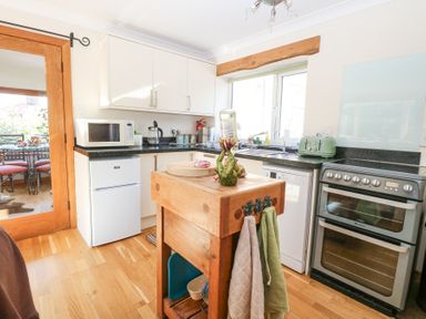 A kitchen with wooden floor white cabinets a wooden island microwave refrigerator oven toaster and window at The Lodge in Coltishall