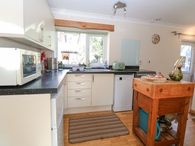 A kitchen with white cabinets black countertops a wooden island and a striped rug at The Lodge in Coltishall
