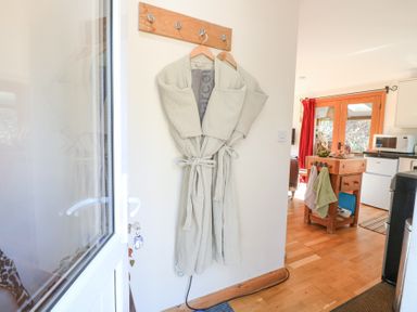 A pair of robes hanging on hooks next to a door with a kitchen area in the background at The Lodge in Coltishall