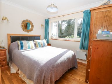 A bedroom with a bed with pillows beside two wooden bedside tables under a window with blue curtains at The Lodge in Coltishall