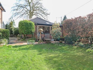 A garden with green grass trees and patio furniture outside a brick house at The Lodge in Coltishall