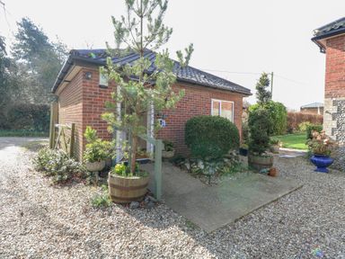 A small brick building with a tiled roof surrounded by potted plants and gravel at The Lodge in Coltishall