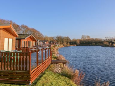 A row of wooden cabins with decks overlooking a body of water and trees at Shore Beats Work - Capenwray 10 in South Lakeland Leisure Village