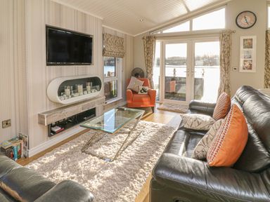 A living room with black leather sofas an orange armchair a glass coffee table and a wall-mounted TV at Shore Beats Work - Capenwray 10 South Lakeland Leisure Village