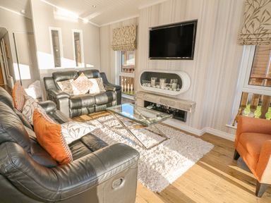 A living room with two black leather sofas a glass coffee table a wall mounted television and an orange armchair at Shore Beats Work - Capenwray 10 South Lakeland Leisure Village