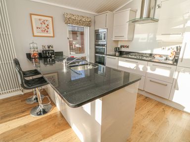 A kitchen with a black countertop island with sink and two black bar stools at Shore Beats Work - Capenwray 10 in South Lakeland Leisure Village