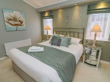 A bedroom with a bed with green and white bedding two bedside tables with lamps and a flower painting on the wall at Shore Beats Work - Capenwray 10 in South Lakeland Leisure Village
