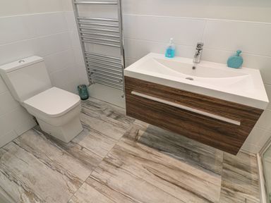 A bathroom with a toilet a towel radiator a wooden vanity unit with a sink and handwash at Shore Beats Work - Capenwray 10 in South Lakeland Leisure Village