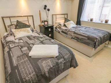 A bedroom with two single beds a nightstand between the beds and a window with curtains at Shore Beats Work - Capenwray 10 in South Lakeland Leisure Village