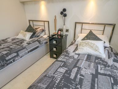 A bedroom with two single beds and a black three-drawer nightstand between them at Shore Beats Work - Capenwray 10 South Lakeland Leisure Village