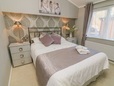 A bedroom with a double bed between two nightstands with lamps and a window on the right at Shore Beats Work - Capenwray 10 in South Lakeland Leisure Village