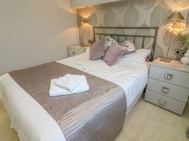 A bedroom with a double bed pillows bedside tables lamps and folded towels at Shore Beats Work - Capenwray 10 South Lakeland Leisure Village