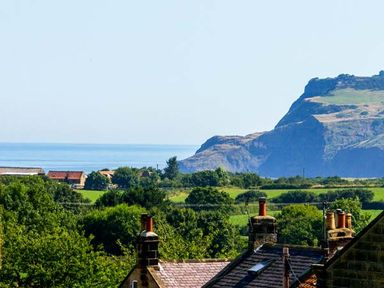 A landscape with rooftops chimneys trees green fields mountains and sea at Croft View in Fylingthorpe near Robin Hood's Bay