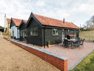 An outdoor dining area with a table and six chairs next to a black wooden building with a red tiled roof at Whitehands Farm Barn in Old Buckenham