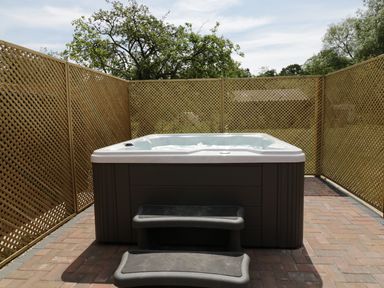 An outdoor hot tub with steps surrounded by lattice fencing and trees at Whitehands Farm Barn in Old Buckenham