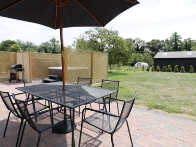 An outdoor patio with a metal table and chairs under a large umbrella next to a wooden fence and barbecue grill at Whitehands Farm Barn in Old Buckenham