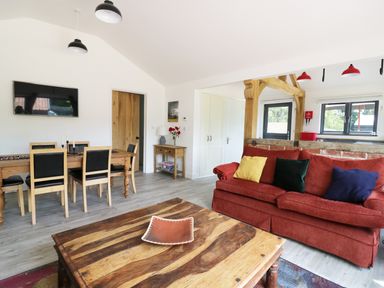A living room with a wooden coffee table red sofa with colored cushions dining table with chairs and a wall-mounted tv at Whitehands Farm Barn in Old Buckenham
