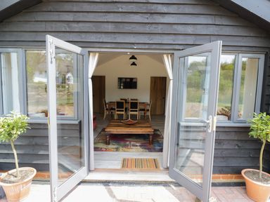 An open glass door leading to a room with a wooden coffee table and dining table with chairs at Whitehands Farm Barn in Old Buckenham