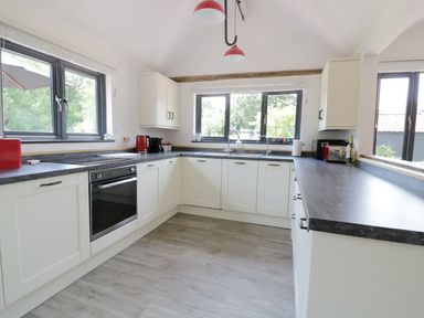 A kitchen with white cabinets gray countertops and windows showing greenery at Whitehands Farm Barn in Old Buckenham