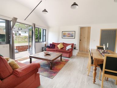 A living room with red sofas a wooden coffee table and a dining table with chairs at Whitehands Farm Barn in Old Buckenham