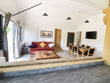 An open living and dining area with a red sofa and wooden table at Whitehands Farm Barn in Old Buckenham