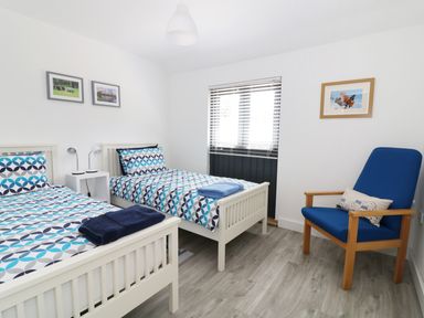 A bedroom with two beds a blue armchair and framed pictures on the walls at Whitehands Farm Barn in Old Buckenham