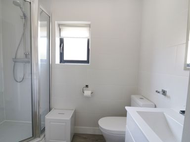 A bathroom with a shower cubicle a toilet a sink a small window and a white storage box at Whitehands Farm Barn in Old Buckenham