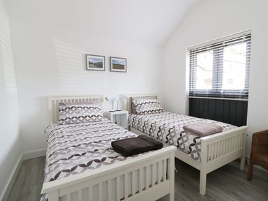 A bedroom with two single beds with patterned bedding and a window with blinds at Whitehands Farm Barn in Old Buckenham