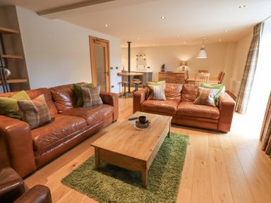 A living room with two leather sofas and a wooden coffee table on a green rug at Yew Cottage in Backbarrow