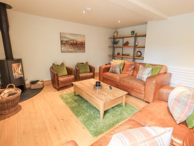 A living room with leather sofas green cushions a wooden coffee table and a wood stove at Yew Cottage in Backbarrow