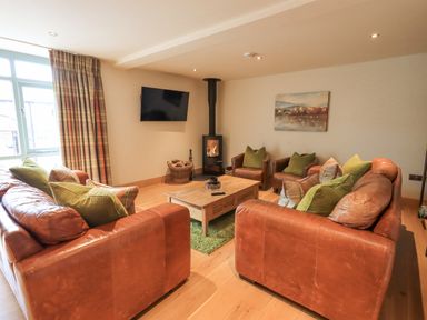 A living room with leather sofas armchairs a wooden coffee table and a wall mounted tv at Yew Cottage in Backbarrow