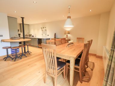 A dining area with wooden table and chairs next to a kitchen with stools and cabinets at Yew Cottage in Backbarrow