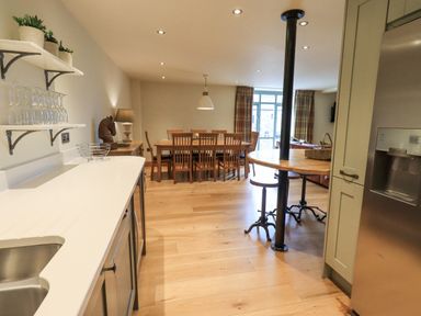A kitchen and dining area with wooden dining table and chairs and a round wooden table with stools at Yew Cottage in Backbarrow