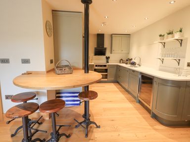 A kitchen with wooden bar stools and a round wooden table at Yew Cottage in Backbarrow