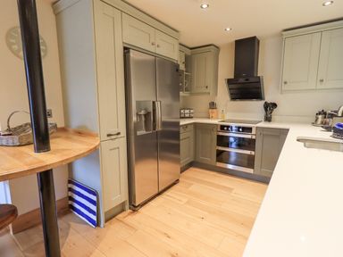 A kitchen with a stainless steel refrigerator an oven a black extractor hood wooden floor and green cabinets at Yew Cottage in Backbarrow