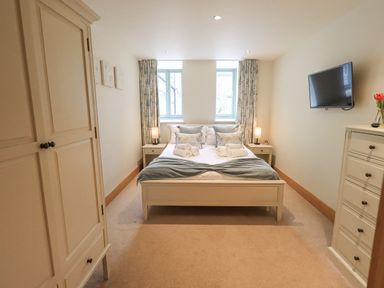 A bedroom with a double bed two bedside tables with lamps a wardrobe a dresser and a wall-mounted TV at Yew Cottage in Backbarrow