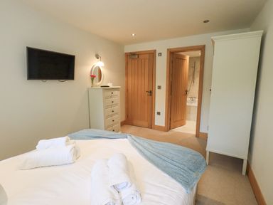 A bedroom with a bed, a wall-mounted TV, a chest of drawers with a mirror and a wardrobe at Yew Cottage in Backbarrow