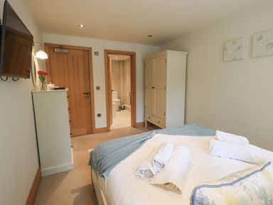 A bedroom with a bed, wardrobe, chest of drawers, and an open door to a bathroom at Yew Cottage in Backbarrow