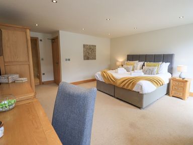 A bedroom with a large bed with pillows and folded towels bedside tables with lamps a chair and wooden furniture at Yew Cottage in Backbarrow