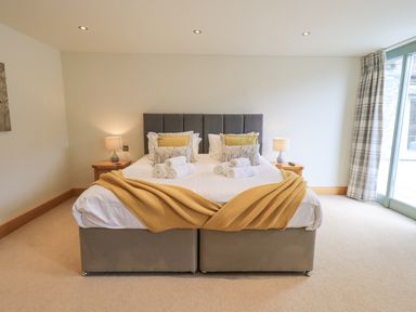 A bedroom with a double bed and pillows two bedside tables with lamps and a window with curtains at Yew Cottage in Backbarrow