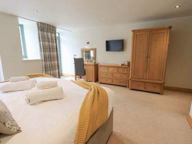 A bedroom with a bed, dresser, wardrobe, desk with chair and a wall-mounted tv at Yew Cottage in Backbarrow